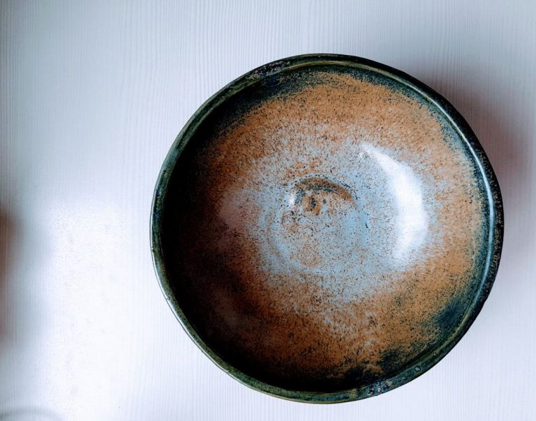 Een close-up van een keramische kom met bruine en blauwe glazuur op een witte ondergrond.