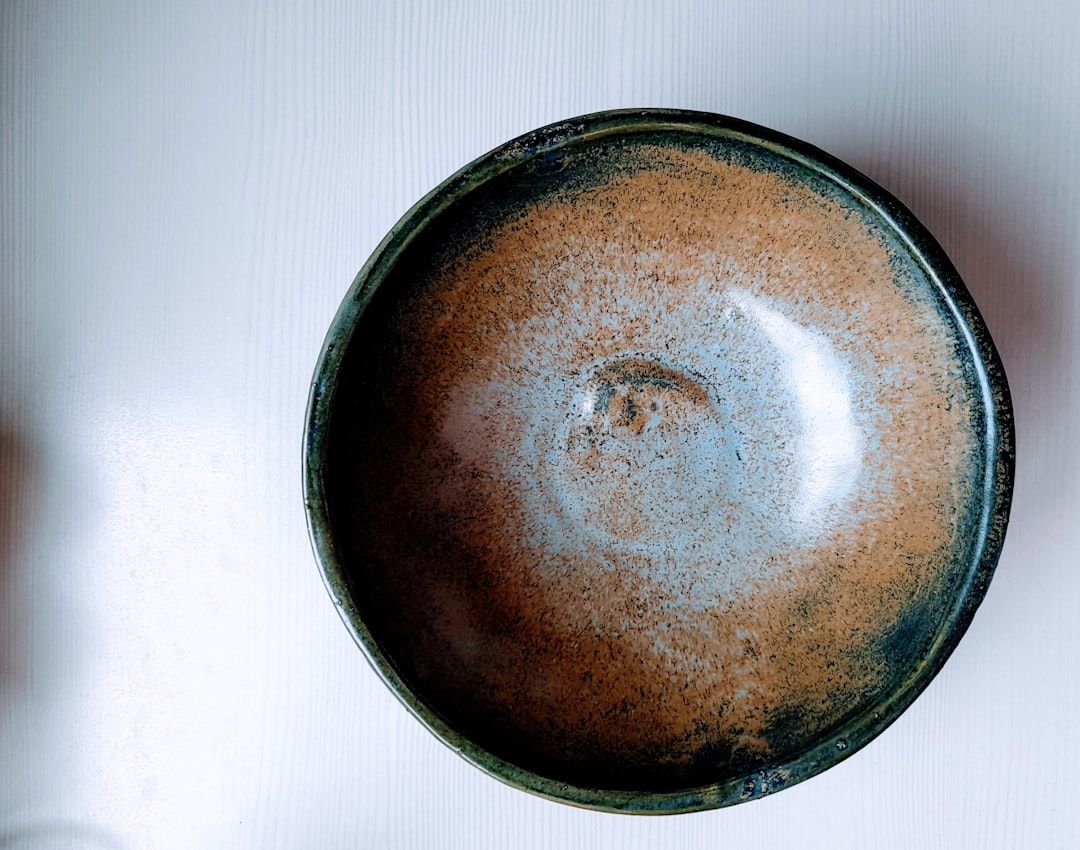 Een close-up van een keramische kom met bruine en blauwe glazuur op een witte ondergrond.