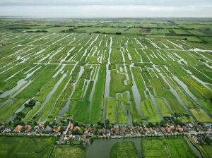 Luchtfoto van een strak verkaveld, waterrijk polderlandschap met dorp